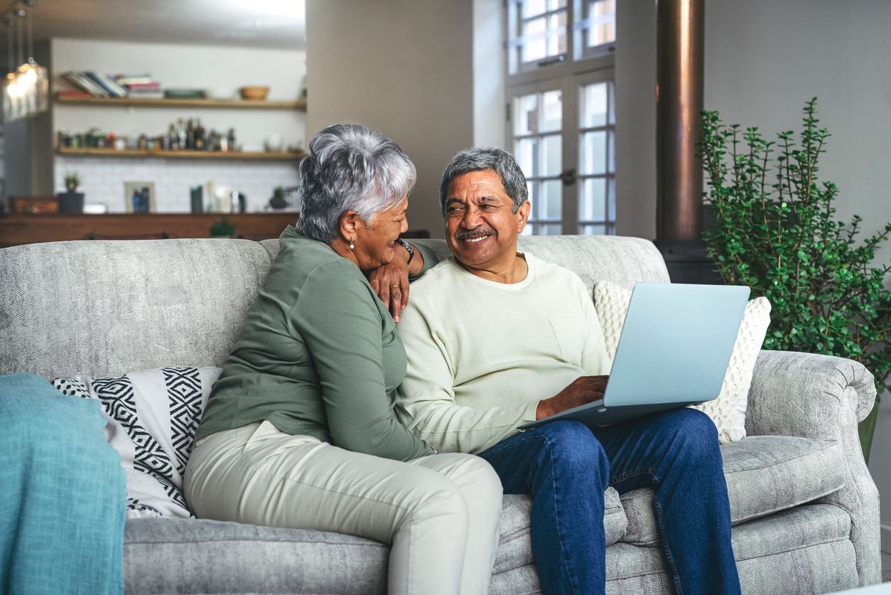 elderly couple sitting on couch with laptop